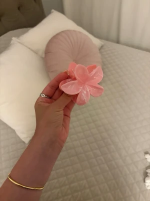 Rosa blomformad hårklämma - Superfin hårklämma i form av en blomma, gjord i glansig rosa plast med marmorerad effekt. Perfekt för att sätta upp håret på ett snyggt och trendigt sätt. Klämman har fem blad och ger en söt och lekfull look.