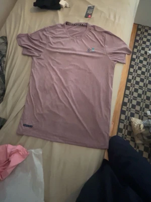 Ljuslila t-shirt med liten logga - Säljer en ljuslila t-shirt med kort ärm och rund hals. T-shirten har en liten broderad logga på bröstet och en diskret etikett nertill. Perfekt för en avslappnad stil.