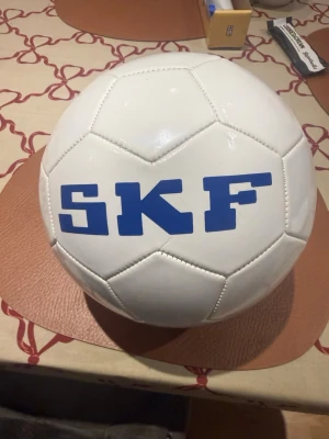 Vit Gothia Cup SKF boll limited edition - Säljer en vit fotboll med blå SKF-tryck och Gothia Cup-logga. Bollen har klassisk design med sydda paneler och är tillverkad i konstläder. Perfekt för dig som gillar fotboll och vill ha en unik boll från Gothia Cup. Man kan inte få den längre pris kan diskuteras 