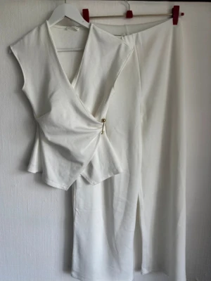 Vitt loungewear-set med omlottopp - Snyggt vitt loungewear-set med ärmlös omlottopp och vida byxor. Setet är gjort i mjukt, stretchigt tyg som känns bekvämt mot huden. Toppen är i storlek M men passar S. Byxorna är normala i storleken 🤍 