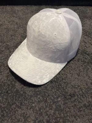 Vit meshkeps med böjd skärm - Snygg vit keps med böjd skärm och meshpaneler på sidorna för extra ventilation. Klassisk trucker-modell med justerbar baksida och stilren look. Perfekt för dig som vill ha en enkel och clean accessoar till din outfit.