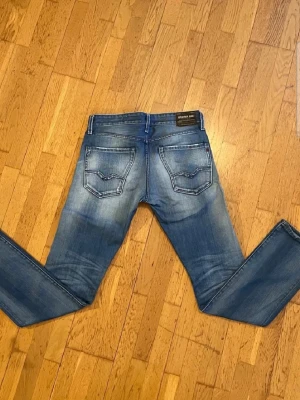 Blå Replay jeans med tvättad look - Säljer ett par blå jeans från Replay med snygg tvättad effekt och klassiska bakfickor med dekorativa sömmar. Jeansen har normal midja och raka ben. Materialet är denim i bomull med lite stretch för extra komfort.