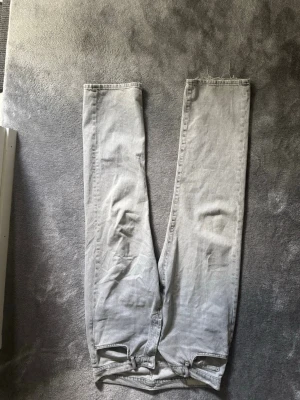 Zara original jeans  - Säljer ett par ljusgrå jeans med rak passform och rå, fransig kant längst ner på benen. Jeansen har en klassisk femficksdesign och är tillverkade i ett mjukt denimtyg. Perfekta för en avslappnad och trendig look.