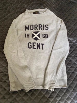 Grå stickad tröja Morris Gents - Snygg grå stickad tröja från Morris Gents med texten 'Morris Gent 1968' och ett broderat skotskt kors på bröstet. Tröjan har rund hals, ribbade muddar och nederkant. Perfekt för dig som gillar klassisk och sportig stil. Tröjan är i storlek M men passar även S. Inga defekter eller slitage. Hör av dig vid frågor!