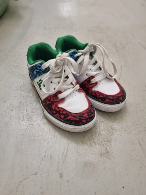 Färgglada låga sneakers med mönster - Snygga sneakers i vitt med färgglada detaljer. Skorna har röd och blå mönstrad kant, grönt foder och vita skosnören. Ovandelen är i syntetmaterial och textil, med perforeringar på tån för extra ventilation. Perfekta för dig som gillar unika och färgstarka skor.