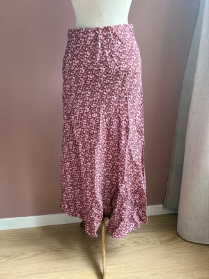 Ny Lång blommig kjol från Odd Molly stl 1 - Lång kjol från Odd Molly i en härlig vinröd nyans med småblommigt mönster i vitt. Kjolen har en mjuk och flowy passform med lätt vågig nederkant. Perfekt för dig som gillar romantisk och bohemisk stil.