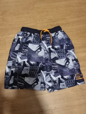 Mönstrade shorts med snörning  - INSTABOX!!! Säljer ett par coola shorts med svartvitt grafiskt mönster och motiv av skateboardåkare. Shortsen har elastisk midja med orange snörning och är tillverkade i ett lätt syntetmaterial, perfekta för sommardagar. I46-152