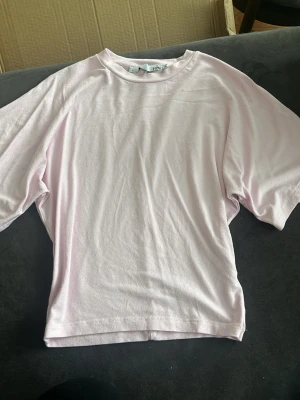 Ljusrosa figursydd t-shirt från 157 - Enkel och stilren ljusrosa t-shirt från 157 med rund hals och korta ärmar. Tillverkad i mjuk bomull som känns skön mot huden. Perfekt basplagg att matcha med jeans eller shorts.