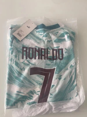 Portugal bortaställ 2026 (Ronaldo)  - Säljer en Portugal matchtröja från Puma med Ronaldo och nummer 7 på ryggen. Tröjan är vit och turkos med grafiskt mönster, korta ärmar och rund hals. Perfekt för dig som älskar fotboll och vill stötta Portugal på match eller träning.