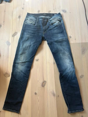Mörkblå slim fit jeans från Replay - Säljer ett par mörkblå slim fit jeans med snygga slitningar och klassisk femficksmodell. Jeansen har en något tvättad look och raka ben. Perfekta för dig som gillar en avslappnad men ändå stilren stil. Storlek 31/32