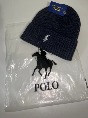 Mörkblå ribbstickad mössa Polo Ralph Lauren - Snygg mörkblå ribbstickad mössa från Polo Ralph Lauren med klassisk broderad logga framtill. Mössan har uppvikt kant och är tillverkad i mjukt material som håller dig varm. Perfekt accessoar för kyliga dagar.