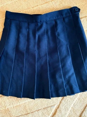 American Apparel Svart/Marinblå Veckad Minikjol, storlek S - Oanvänd!  Strl.Small (midjemått 35 cm, mätt rakt över)  Har svårt att avgöra ifall den är djupt mörkblå eller svart, men mer åt det svarta hållet!  ”Klassisk plisserad kjol i mörkblått/svart. Kjolen har en tidlös design med veck som ger den volym och rörelse. Den är försedd med en knapp i midjan för enkel knäppning. Passar utmärkt för en mängd olika tillfällen, från vardagsbruk till mer uppklädda evenemang.”  Nypris 899kr  Se gärna mina övriga annonser för bundlerabatter och samfrakt!