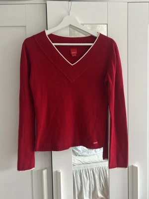 Röd stickad tröja från Esprit - Röd stickad tröja från Esprit med V-ringning och vita detaljer längs halsringning och ärmslut. Tröjan har långa ärmar och är perfekt för lager-på-lager. Materialet känns mjukt och bekvämt. Lite smått nopprig på vissa ställen men i väldigt fint skick.