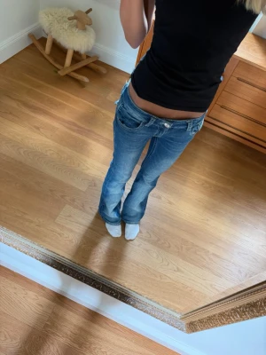 Blå low waist bootcut jeans - Säljer ett par blå low waist jeans med bootcut passform. Jeansen har detaljerade bakfickor med lock och knapp. Perfekta för dig som gillar en avslappnad men trendig look.💕