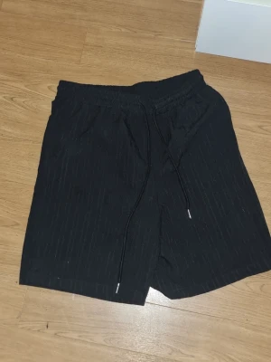 Svarta shorts  - INSTABOX!!! Säljer ett par svarta shorts med elastisk midja och dragsko. Shortsen har en enkel design och är tillverkade i ett lätt tyg som passar perfekt till sommaren. Inga synliga loggor eller märken. Klassisk passform och raka ben.