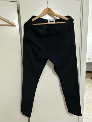 Svarta chinos från Les Deux - Snygga svarta chinos från Les Deux med klassisk rak passform och diskret dragkedja. Byxorna är tillverkade i ett mjukt och bekvämt tyg som passar perfekt till en stilren look. Tillverkade i Turkiet.