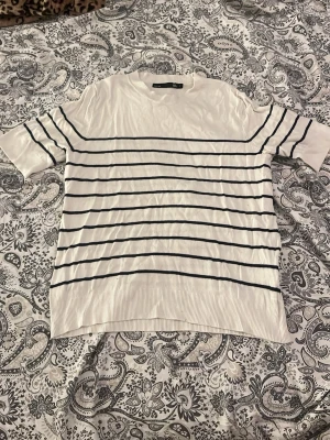 Vit randig topp med kort ärm - Vit topp med tunna svarta horisontella ränder och korta ärmar. Tillverkad i ett mjukt och tunt material som känns skönt mot huden. Perfekt till jeans eller kjol för en enkel och stilren look.💗