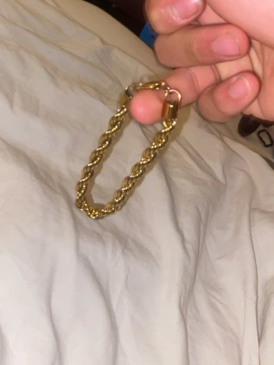 Guldigt tvinnat armband - Snyggt armband i guldfärgad metall med tvinnad design. Armbandet har en robust känsla och ett klassiskt lås. Perfekt accessoar för att lyfta din stil med en touch av guld.