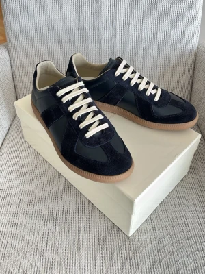 Navy Maison margiela gats - Säljer ett par snygga navy Maison margiela gats med mockadetaljer och vita snören. Skorna har en klassisk låg siluett och brun gummisula. Materialmix av mocka och slätt läder ger en stilren look som passar till det mesta. Tveka inte att höra av er vid frågor🙌 pris är diskuterbart💸