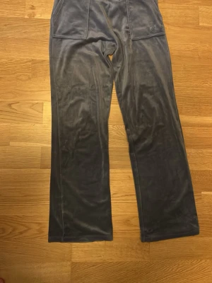 Blå/lila velour mjukisbyxor - Säljer ett par blå/lila mjukisbyxor i mjuk velour med bred resårmidja och snörning med guldfärgade detaljer. Byxorna har raka ben och stora fickor framtill. Perfekta för chill dagar eller när du vill vara extra bekväm. Har en liten fläck men går nog bort i tvätten inget som märks.