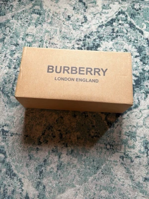 Burberry tofflor - Säljer ett par Burberry tofflor i storlek 43. Sandalerna har ett klassiskt svart band med Burberrys ikoniska beige, röda och svarta rutmönster. Perfekta för sommaren och tillverkade i slitstarkt material för en trendig look.