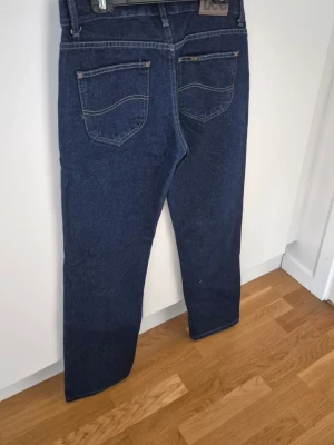 Lee Baggy Jeans - Snygga mörkblå jeans från Lee med klassisk baggy passform. Jeansen har fem fickor, bälteshällor och stängs med dragkedja och knapp. Materialet är kraftig denim som ger en tidlös look. Perfekta för dig som gillar enkel och stilren stil.