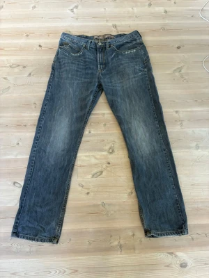 Blå raka/bootcut jeans med slitningar från wrangler - Ett par klassiska blå jeans med rak/bootcut passform och diskreta slitningar på benen. 