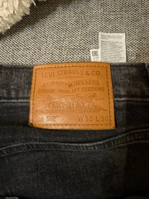 Levi's 502 svarta jeans W30 L30 - Säljer ett par svarta Levi's 502 jeans i storlek W30 L30. Jeansen har klassisk femficksdesign, rak passform och är tillverkade i slitstark denim. Perfekta för dig som gillar en tidlös och avslappnad stil.