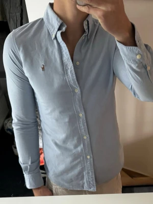 Ljusblå skjorta med knappar - Säljer en stilren och klassisk skjorta från Ralph Lauren. Perfekt för både vardag och mer uppklädda tillfällen.  Storlek: S Passform: slim fit Färg: blå Skick: mycket bra  Skjortan är tillverkad i högkvalitativt material och har den ikoniska Ralph Lauren-loggan broderad på bröstet.  Hör av dig vid intresse eller frågor!