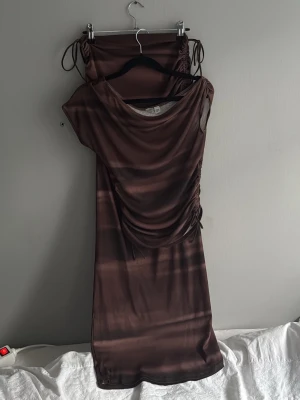 Brunt set med snörnings detaljer - Säljer ett brunt set med omlottdetalj och snörning i sidan. Klänningen har ett mjukt, stretchigt material och subtila ränder i olika bruna nyanser. Perfekt för dig som gillar trendiga och unika plagg.