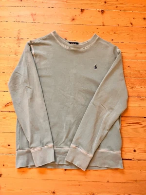 Grön sweatshirt från Polo Ralph Lauren - Ljusgrön sweatshirt från Polo Ralph Lauren med klassisk rund halsringning och broderad logga på bröstet. Tröjan har långa ärmar och ribbade muddar vid ärmslut och nederkant. Perfekt för en avslappnad och stilren look.