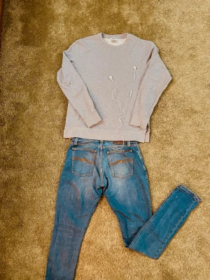Acne Studios  - Säljer en stilren grå sweatshirt från Acne Studios. Tröjan har rund hals, långa ärmar och ribbade muddar vid ärmslut och nederkant. Tillverkad i mjuk bomull för en skön känsla. Enkel och clean design. En liten dragkedja på vardera sida. Storlek = S  Hör av er vid frågor! Priset kan diskuteras. Säljer även jeansen på mitt konto! 