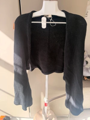 Svart stickad bolero - Snygg svart stickad bolero med lång ärm och öppen front. Perfekt att slänga över en topp eller klänning för en extra touch. Tunn och mjuk kvalitet som ger en avslappnad men ändå stilren look.