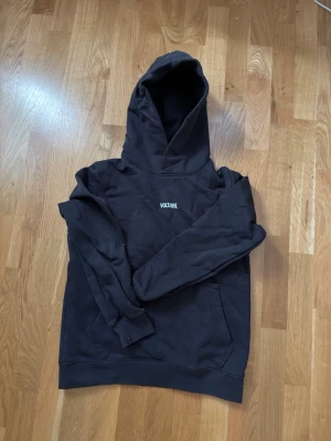 Svart hoodie med tryck från Zadig Voltaire unisex - Svart hoodie med huva och ficka framtill. På bröstet står det 'VOLTAIRE' i vitt och på ryggen finns ett stort tryck med texten 'STAY WITH ME' och en grafisk illustration i blått och vitt. Tillverkad i mjukt bomullsmaterial och har ribbade muddar.