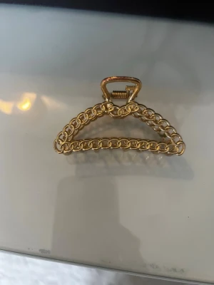 Guldig hårklämma i kedjedesign - Snygg hårklämma i metall med guldfinish och trendig kedjedesign. Triangelformad och perfekt för att hålla upp håret på ett stilrent sätt. Ger en lyxig touch till din look och är enkel att använda.