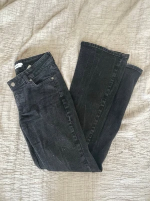 Svarta raka jeans med låg midja - Säljer ett par svarta bootcut jeans som är lowwaisted. Jeansen har klassisk femficksdesign, bälteshällor och knappgylf. Tvättad svart färg.