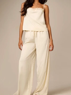 Krämfärgat loungewear-set med spets - Säljer ett krämfärgat loungewear-set med linne och vida byxor. Linnet har tunna axelband och spetsdetalj vid urringningen. Byxorna har resår i midjan för extra komfort. Materialet ser mjukt och glansigt ut, perfekt för chill dagar hemma.