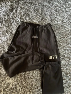 Svarta Essentials mjukisbyxor 1977 - Snygga svarta mjukisbyxor från Essentials med trycket '1977' på benet och dragsko i midjan. Byxorna har elastisk midja och muddar vid benslut. Perfekta för en chill och avslappnad stil.