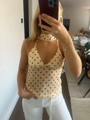 Prickig beige mesh linnetopp - beige mesh linnetopp med bruna prickar och smala axelband. Toppen har en djup v-ringning och scarf som sitter fast i toppen och knyts runt halsen. 💛 aldrig använd