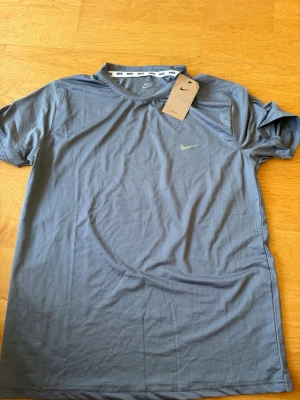 Blå Nike Dri-Fit träningströja - Snygg blå kortärmad träningströja från Nike med Dri-Fit-teknologi som håller dig torr under träningspasset. Tröjan har rund hals, diskret Nike-logga på bröstet och är tillverkad i ett lätt och ventilerande material.