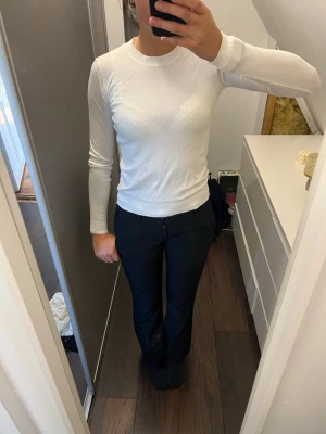 Vit stickad tröja från 157 - Klassisk vit stickad tröja från 157 med rund halsringning och långa ärmar. Tröjan har en smal passform och ribbade muddar vid hals, ärmslut och nederkant. Perfekt basplagg till garderoben.