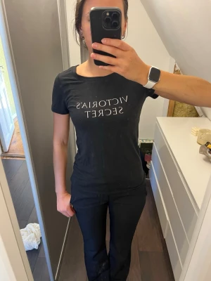 Svart t-shirt från Victoria's Secret - Snygg svart t-shirt från Victoria's Secret med vit text på bröstet. Klassisk rund halsringning och korta ärmar. Tillverkad i mjuk bomull som känns skön mot huden. Perfekt till vardags eller att sova i. 