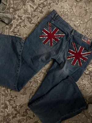 Dolly & Pops jeans med Union Jack-detaljer - Unika blå jeans från Dolly & Pops med stora Union Jack-flaggan på bakfickorna. Klassisk femficksmodell i denim med raka ben och coola detaljer som sticker ut. Perfekta för dig som vill ha en statement-piece i garderoben.