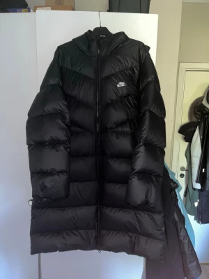 Svart dunjacka lång från Nike - Tja, säljer denna varma vinterjackan från märket Nike. Jackan användes knappt under vintern och säljer den pågrund av att den är en aning stor på mig. Jackan är i storlek L men den kan potentiellt passa en person som bär XL. Den är i 10/10 skick, har inga skador eller så och är använd max 4-5 gånger. I annonsen så finns bilder med jackan på och jag är 180cm samt väger 80kg. Om du har frågor eller är intresserad så är det bara att höra av dig🤝