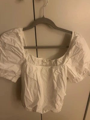 Vit puffärm blus med fyrkantig ringning - Söt vit blus med puffiga korta ärmar och fyrkantig ringning. Blusen har resår vid ärmslut och nederkant för en skön passform. Perfekt till jeans eller kjol🤍