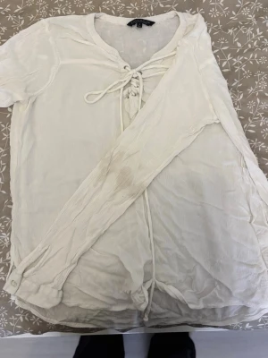 Vit blus med snörning från Soulriver - Vit blus från Soulriver i storlek M. Blusen har långa ärmar och snörning framtill vid halsen. Tillverkad i ett lätt och luftigt tyg som ger en avslappnad känsla. Finns fläckar på armen som jag tror går bort i tvätten med rätt medel och temp. Säljs då det inte är riktigt min stil längre