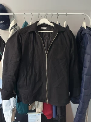 Svart jacka från J.Lindeberg - Stilren svart jacka från J.Lindeberg med dragkedja framtill och klassisk krage. Jackan har en bröstficka och raka ärmar. Perfekt för dig som gillar minimalistisk design och enkelhet.
