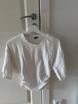 Vit croppad t-shirt - Säljer en enkel vit croppad t-shirt i mjuk bomull. T-shirten har rund halsringning och korta ärmar, perfekt till jeans eller kjol. Passformen är loose och tyget känns lätt och bekvämt. Den är ganska kort så den kan liknas vid en magtröja.