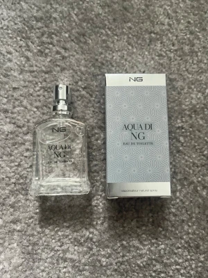 NG Aqua De NG Eau de Toilette (15ml) - Fräsch parfym från NG, Aqua di NG Eau de Toilette. Flaskan är transparent med silverfärgad spray och har en stilren, modern design. Förpackningen är ljusgrå med subtilt mönster och silverdetaljer. Perfekt för dig som gillar lätta och fräscha dofter.