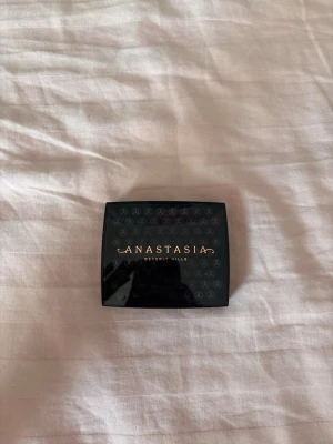 Svart sminkspegel Anastasia Beverly Hills - Snygg och kompakt sminkspegel från Anastasia Beverly Hills i svart plast med guldfärgad logga på locket. Spegeln är fyrkantig och perfekt att ha med i väskan för snabba touch-ups. Praktisk och stilren design som känns lyxig.